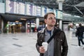 Smiling thoughtful man in front of arrivals and departures board at the airport with a coffee Royalty Free Stock Photo