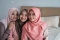 Smiling three hijab women sitting on the bed in the bedroom