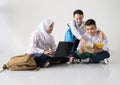 smiling three teenagers in junior high school uniforms sitting on the floor studying together using a laptop and a book Royalty Free Stock Photo