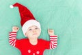 Smiling toddler boy lying on green coverlet. Christmas baby wearing big red Santa hat looking at camera. New Year