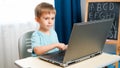 Smiling toddler boy opens laptop and turn it on. Child using computers and gadgets for education and doing homework. Royalty Free Stock Photo