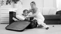 Cute smiling toddler boy sitting in suitcase while mother packing things for traveling