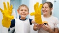 SMiling toddler boy wearing yellow rubber gloves laughing while doing housework and home cleanup