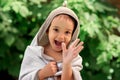 Smiling toddler boy wrapped in big bathing towel after swimming in outdoor pool. Happily laughing child waving hand in summer day Royalty Free Stock Photo