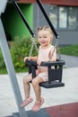 Smiling toddler girl swinging on playground swing. Kid playing on school or kindergarten yard Royalty Free Stock Photo