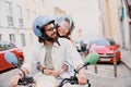 Smiling tourist couple in protective hats are riding on rental vintage scooter in the Lisbon street Royalty Free Stock Photo