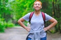 A smiling tourist girl stands on a forest path. A backpack is slung over his shoulders