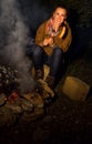 Smiling traveller woman by bonfire grilling sausage