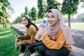 smiling two asian Muslim girls drinking water using bottles after sports together in the afternoon Royalty Free Stock Photo