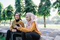 smiling two asian Muslim girls using a handphone together when holding a bottles after sports together in the afternoon Royalty Free Stock Photo