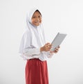 smiling a veiled girl in elementary school uniform stands holding a digital tablet