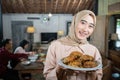 smiling veiled woman carrying a plate of fried chicken with family members eating together