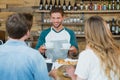 Smiling waiter serving cup of coffee to customers at counter Royalty Free Stock Photo