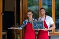 Smiling waitress and waiter standing with open sign board outside cafÃÂ© Royalty Free Stock Photo