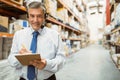 Middle-aged male wearing tie doing warehouse aisle inventory with clipboard and headset, copy space Royalty Free Stock Photo