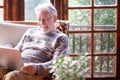 Smiling white haired senior man in winter sweater sitting in living room using laptop computer. Carefree elderly grandfather Royalty Free Stock Photo
