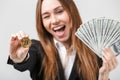 Smiling winking woman showing bitcoin and olding dollars in hands isolated