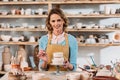 smiling woman in apron painting ceramic dishware