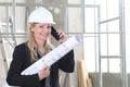 Smiling woman architect or construction engineer talk on the mobile phone wear helmet and holds blueprint inside a building site Royalty Free Stock Photo