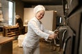 Smiling woman baker opening big industrial oven at modern bakery kitchen