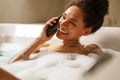 Smiling woman, barechested, gestures happily while talking on phone in bathtub Royalty Free Stock Photo