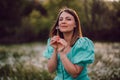 Smiling woman beautiful blowing on ripened dandelion in park. Girl in retro turquoise dress enjoying summer in Royalty Free Stock Photo