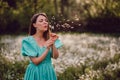 Smiling woman beautiful blowing on ripened dandelion in park. Girl in retro turquoise dress enjoying summer in Royalty Free Stock Photo