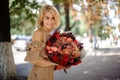Smiling woman in beige dress holds in her hand bouquet of bright red flowers. Royalty Free Stock Photo