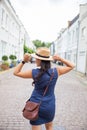 Smiling Woman in Blue Dress From Behind, Calmly Adjusts Her Hat with Both Hands