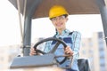 Smiling woman builder in helmet driving construction equipment