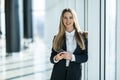 Smiling business woman standing in office with mobile phone in hand looking at camera Royalty Free Stock Photo