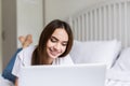 Smiling woman catching up on her social media as she relaxes in bed with a laptop computer on a lazy day Royalty Free Stock Photo