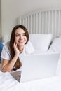 Smiling woman catching up on her social media as she relaxes in bed with a laptop computer on a lazy day Royalty Free Stock Photo