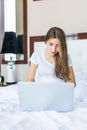 Smiling woman catching up on her social media and relaxes in bed with a laptop computer on a lazy day Royalty Free Stock Photo