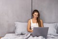 Smiling woman catching up on her social media as she relaxes in bed with a laptop on a lazy day Royalty Free Stock Photo