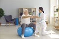 Smiling woman chiropractor correcting old man movements during rehabilitation theapy on fitness ball