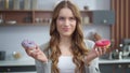 Smiling woman choosing between two donuts at home. Girl having fun with cakes. Royalty Free Stock Photo