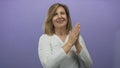 Smiling woman clapping bare hands in purple studio setting with relaxed posture; happiness celebration optimism Royalty Free Stock Photo