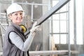 Smiling woman construction worker builder portrait wearing white helmet and hearing protection headphones, holding a metal stud