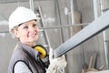 Smiling woman construction worker builder portrait wearing white helmet and hearing protection headphones, holding a metal stud