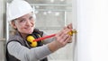 Smiling woman construction worker work with meter tape and pencil, measure wall in interior building site, wearing helmet, glasses