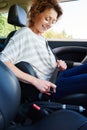 Smiling woman with curly hair buckling seat belt in car