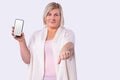 Smiling woman cut blond hair in a white long cardigan holding mobile phone and reached out into a fist.