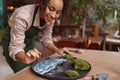 Smiling woman decorator making green ikebana on tray with epoxy resin in florist workshop