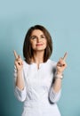 Smiling woman dentist, doctor orthodontist in white medical uniform stands pointing up with both hands