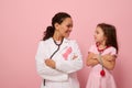 Smiling woman doctor and cute baby girl looking at each other, wearing pink ribbon, symbol of Breast Cancer Awareness Day, Royalty Free Stock Photo