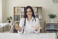 Smiling woman doctor looking at camera and showing something with hands in medical clinic Royalty Free Stock Photo