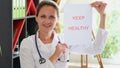 Smiling woman doctor shows inscription keep patient healthy