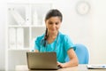 Smiling woman doctor using laptop sitting at desk in medical office Royalty Free Stock Photo