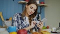 Smiling woman doing online shopping using smartphone and credit card while have breakfast in the kitchen at home